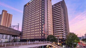 Un hôtel moderne, reconnaissable à son enseigne imposante, doté de plusieurs étages et relié à un autre bâtiment par un pont piétonnier.