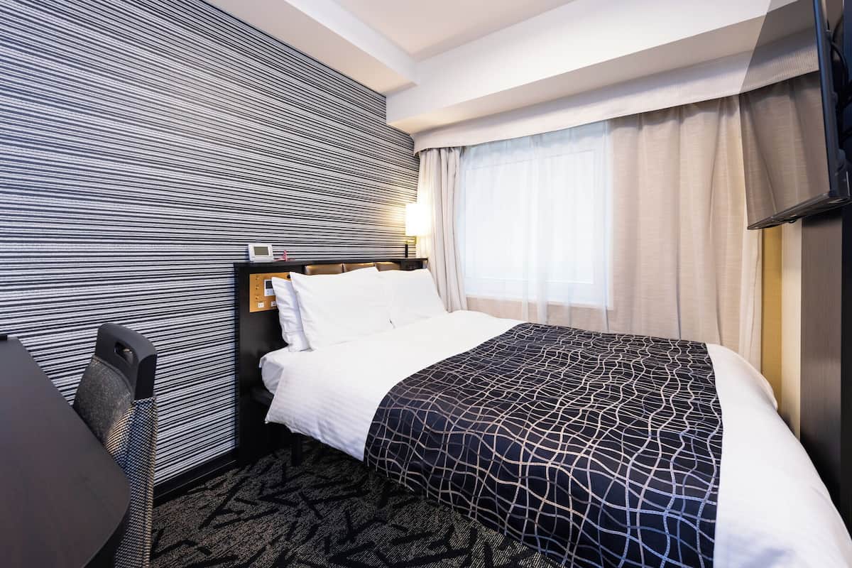 A hotel room with a bed, a desk, and a headboard with controls.