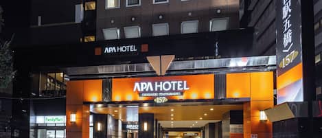 The APA HOTEL entrance with a modern design, featuring a prominent sign and a FamilyMart convenience store nearby.