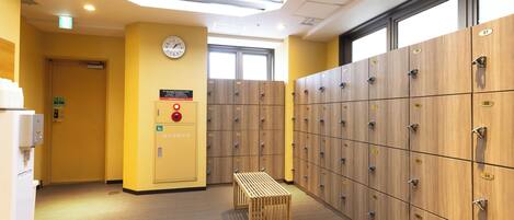 Un hall d’hôtel avec une rangée de casiers en bois, une horloge au mur et un détecteur d’incendie.