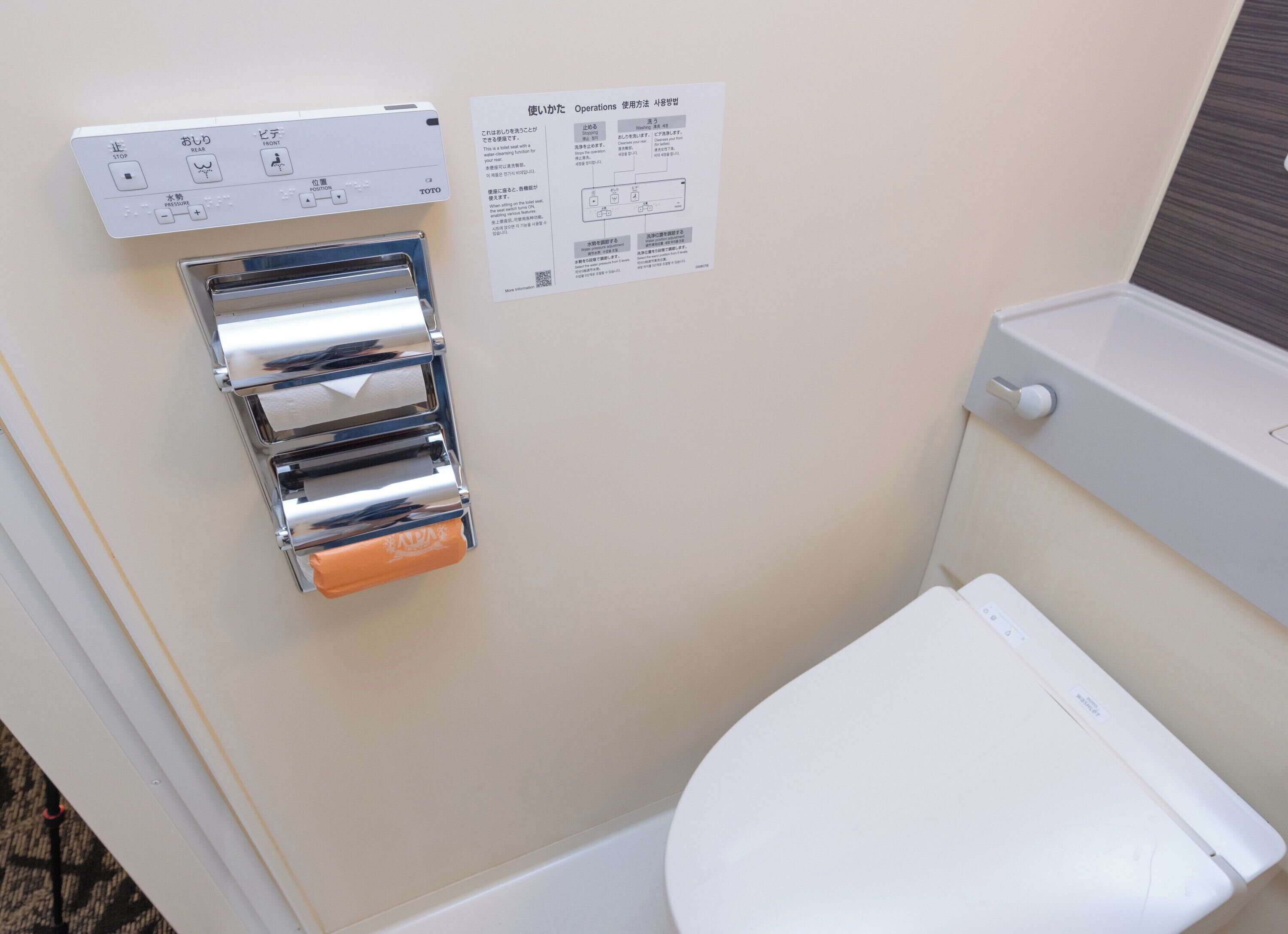 A bathroom with a toilet, a hand dryer, and a paper towel dispenser.