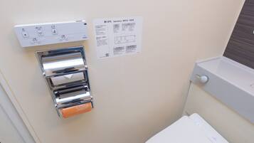 A bathroom with a toilet, a hand dryer, and a paper towel dispenser.