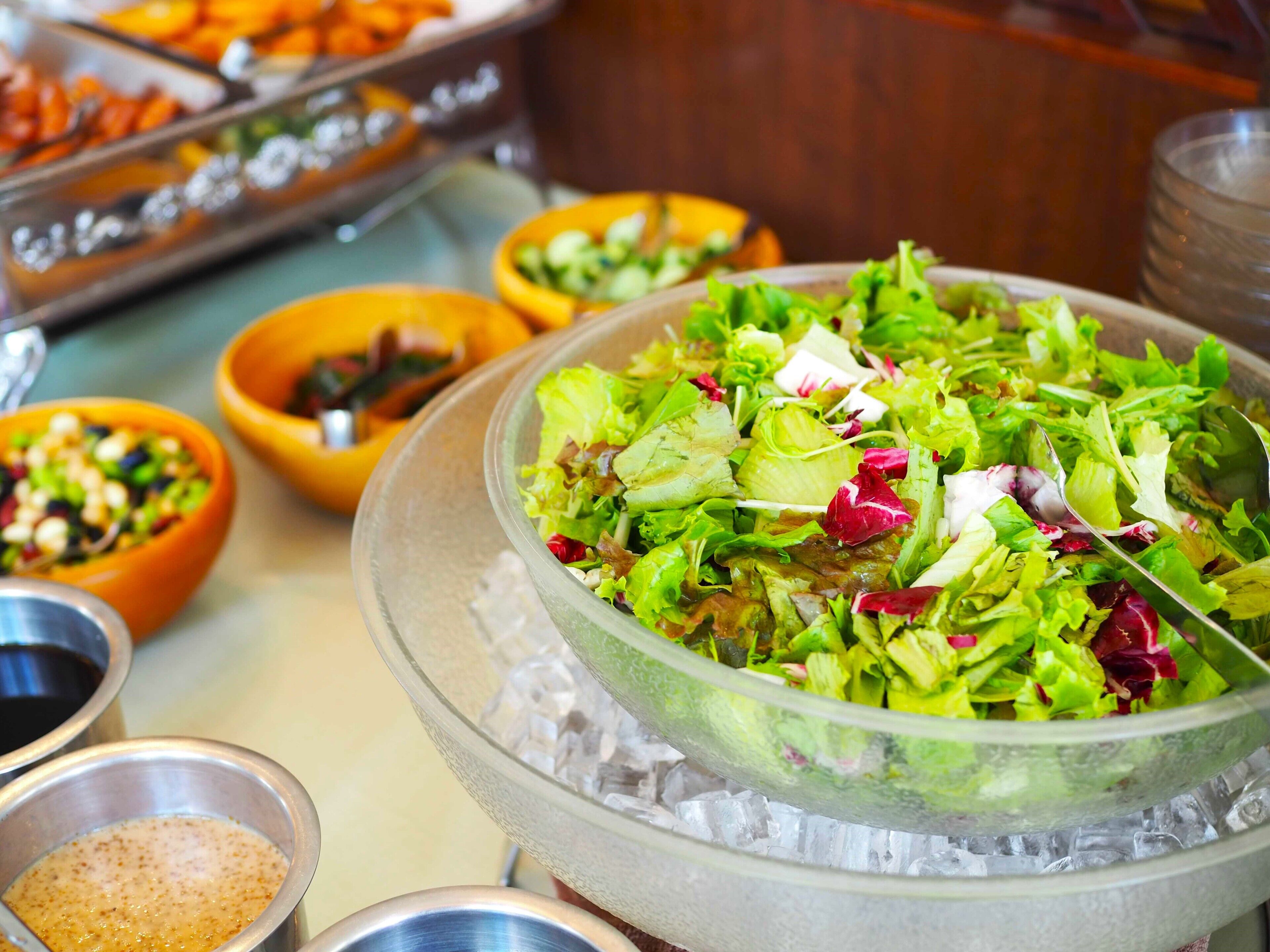 Buffet com diversos pratos, incluindo uma grande saladeira sobre gelo, rodeada por pequenas tigelas com diferentes alimentos.