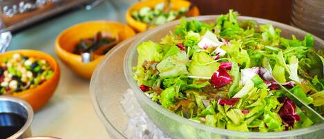 Buffet com diversos pratos, incluindo uma grande saladeira sobre gelo, rodeada por pequenas tigelas com diferentes alimentos.