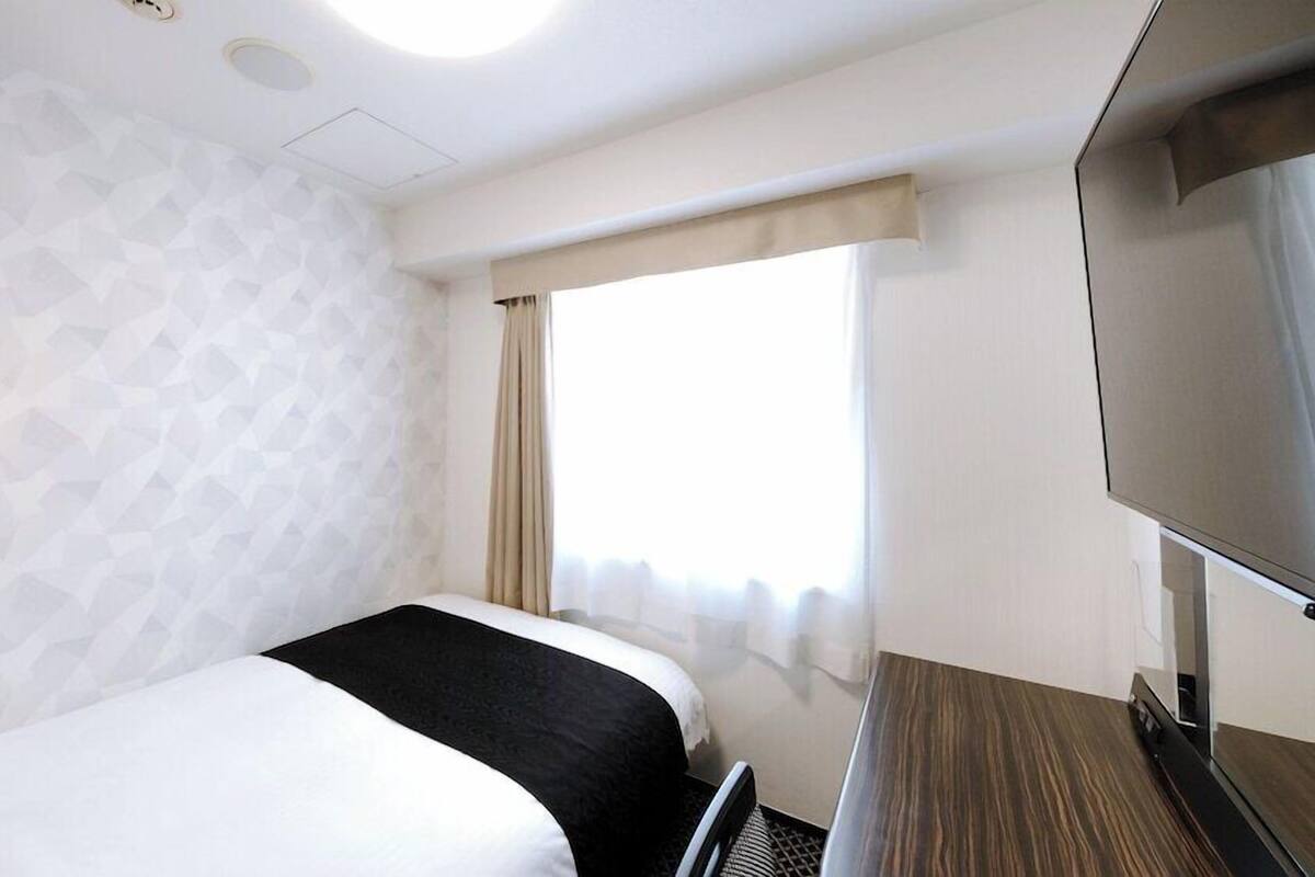 Una habitació d'hotel amb un llit, una televisió, una finestra amb cortines i una paret amb disseny.