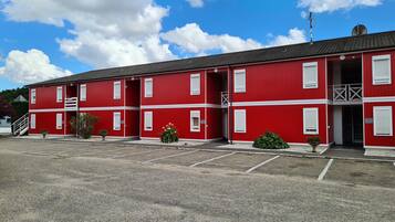 Een rood gebouw met witte details, een parkeerplaats en een blauwe lucht met wolken.