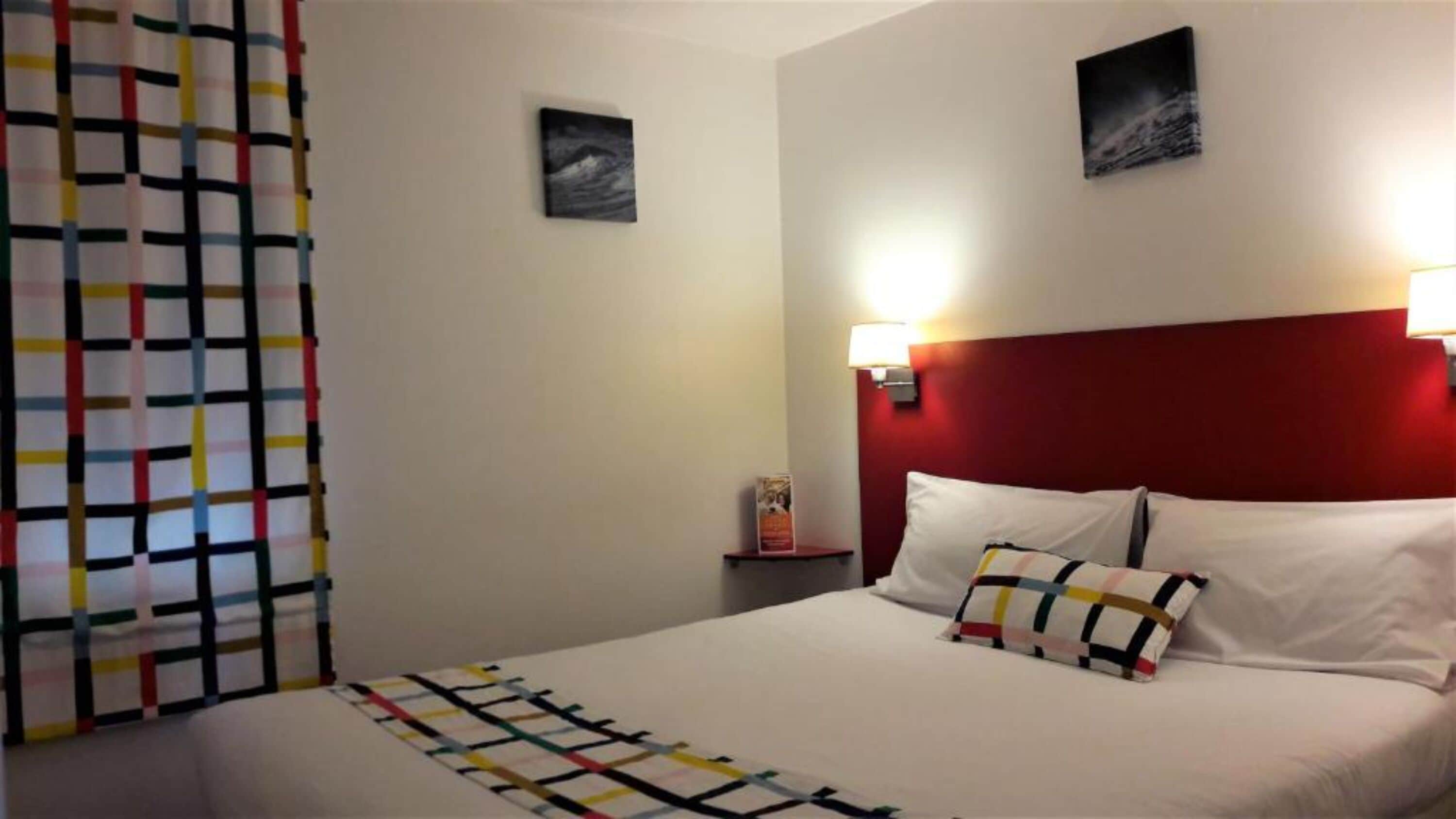A hotel room with a bed, a nightstand, a wall-mounted lamp, and a painting.