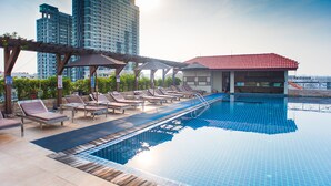 A rooftop pool with lounge chairs, a small building with a red roof, and high-rise buildings in the background. - Intimate Hotel Pattaya (Pattaya)