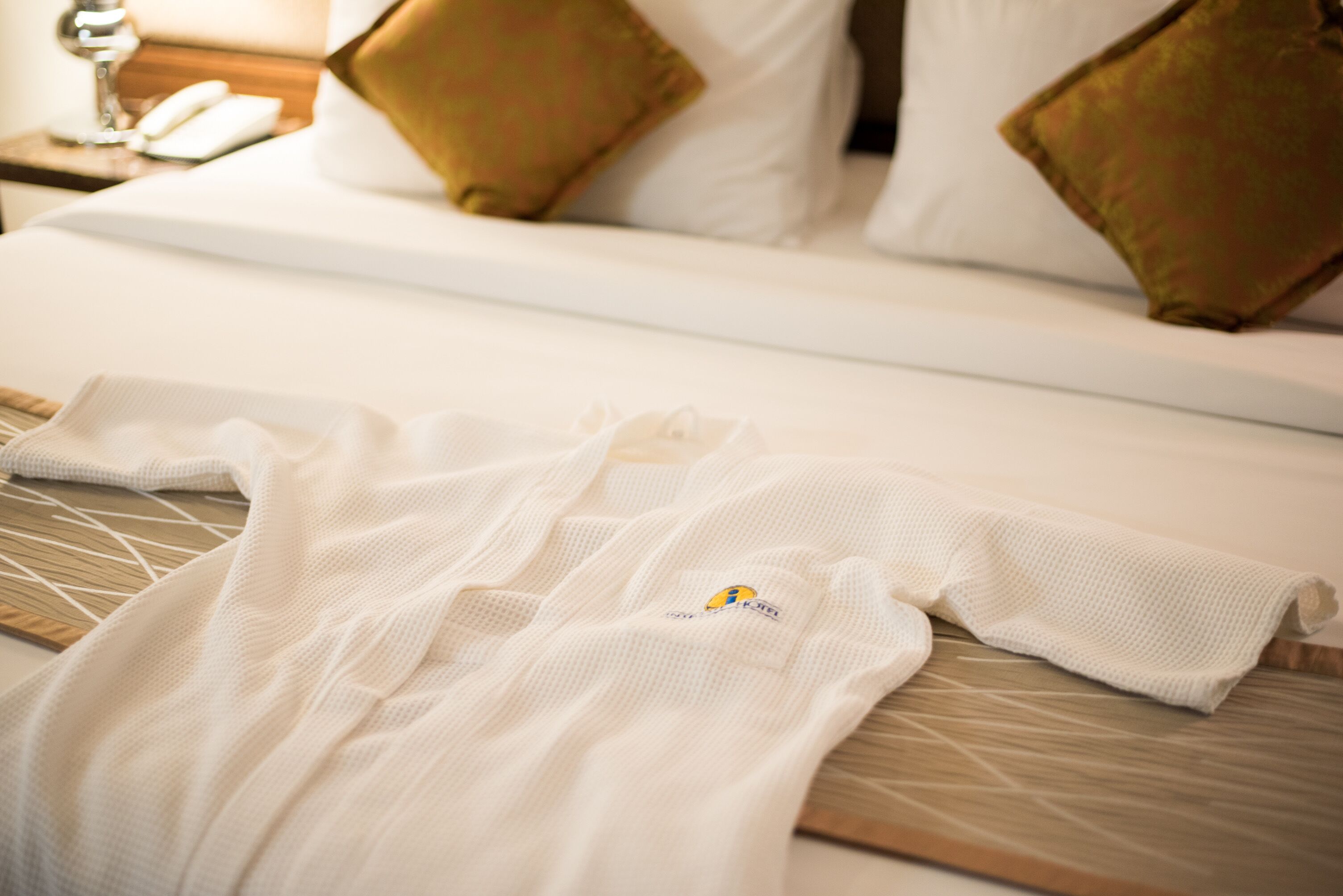 A neatly made bed with white linens and a white robe on the bed.