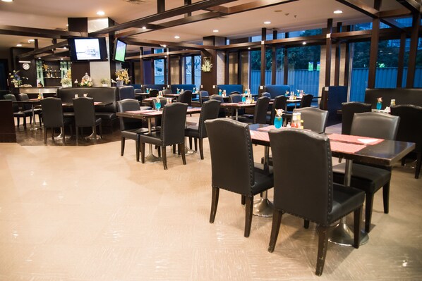 A restaurant with multiple tables and chairs, a TV mounted on the wall, and large windows.