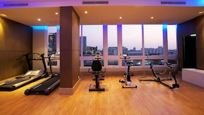 A modern gym with exercise equipment, large windows, and a city view. - Intimate Hotel Pattaya (Pattaya)