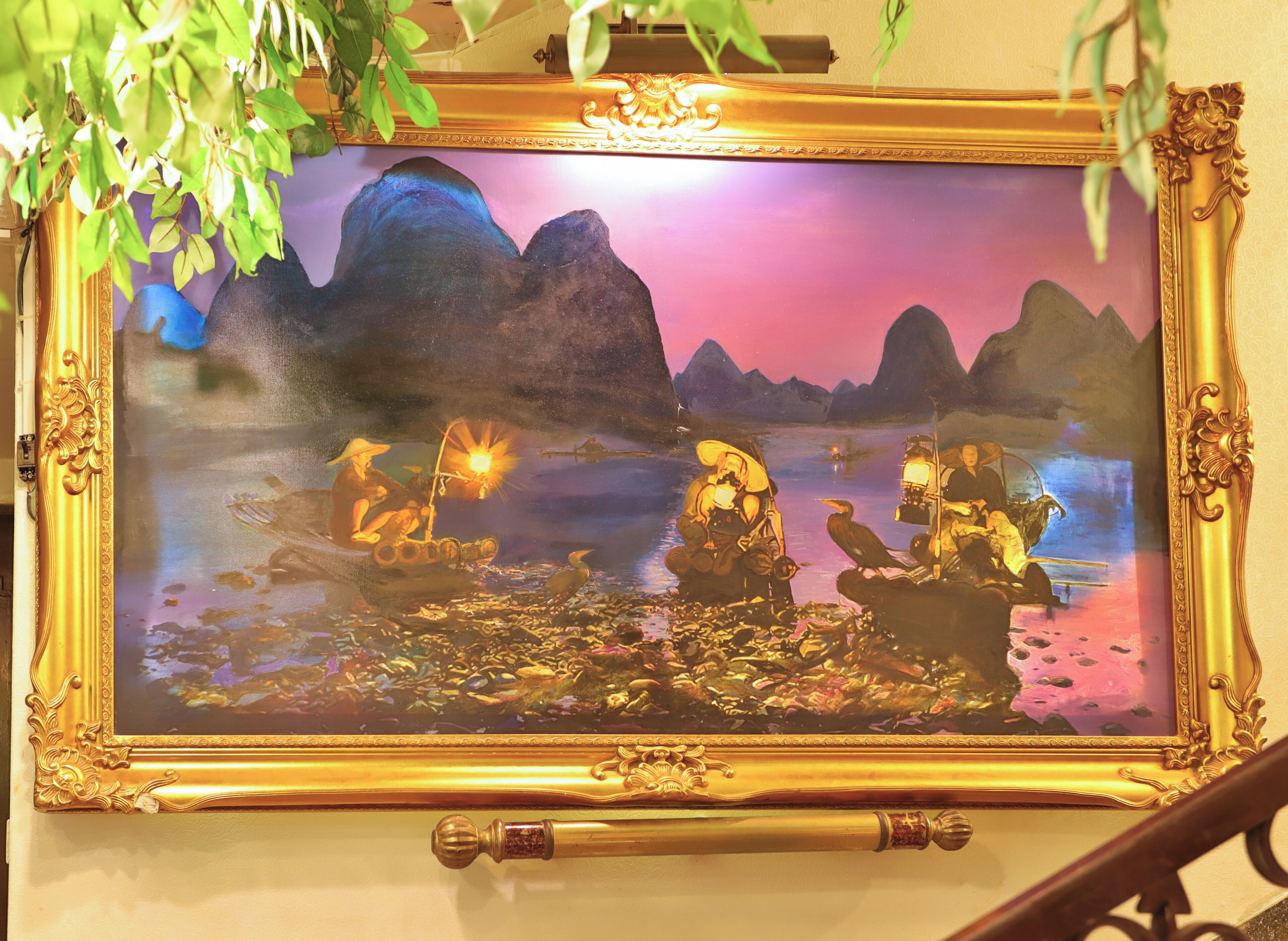 A framed painting with a mountainous landscape and figures in boats, displayed on a wall.