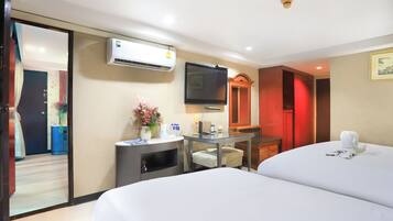 Habitación de hotel con dos camas, un escritorio con silla, un equipo de aire acondicionado, un televisor y una puerta iluminada en rojo.