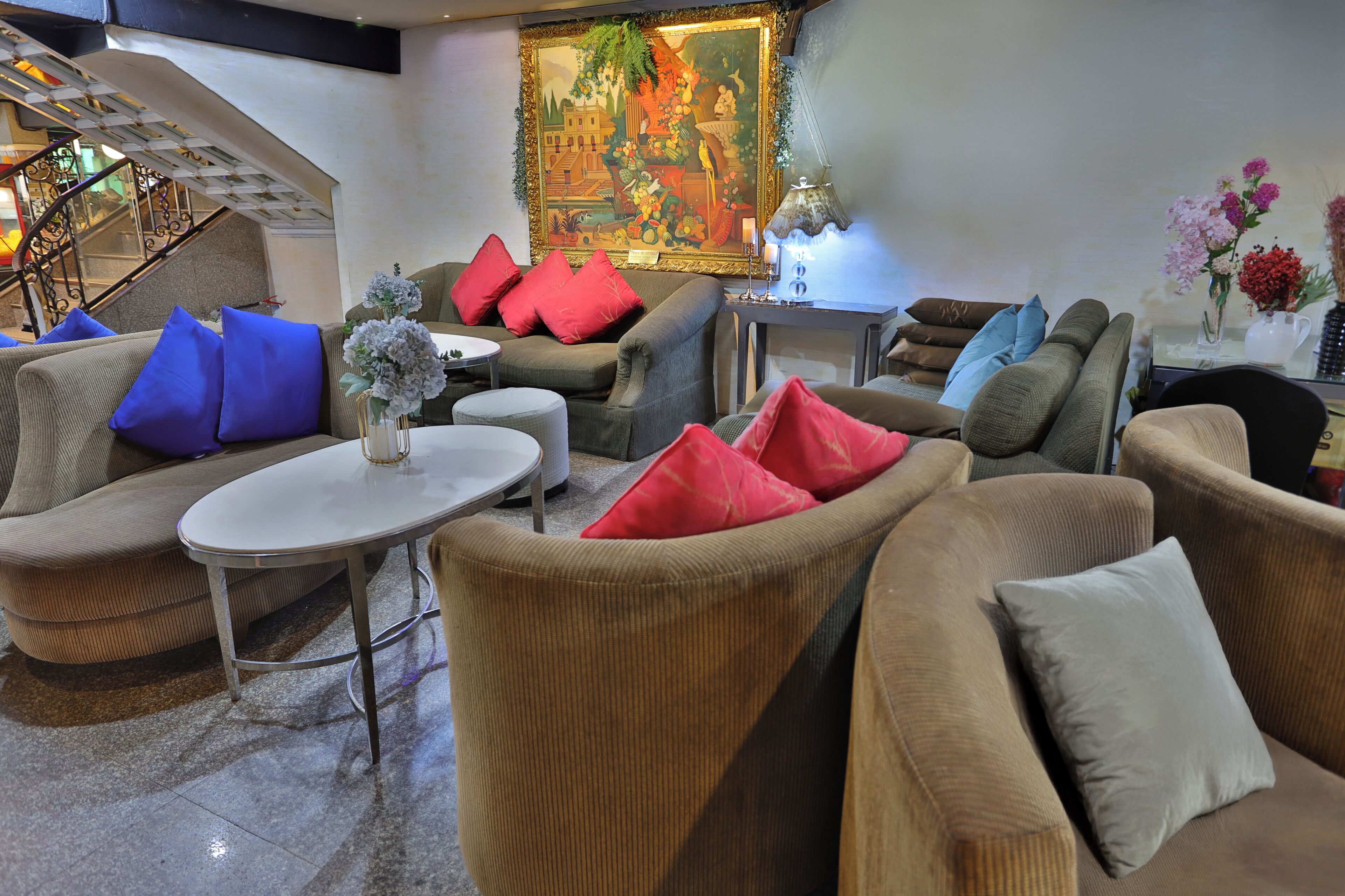 Un hall d’hôtel avec un escalier, un espace salon comprenant plusieurs canapés et fauteuils, une table et un tableau décoratif au mur.