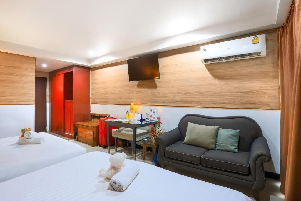 A hotel room with two beds, a sofa, a desk, and a TV.