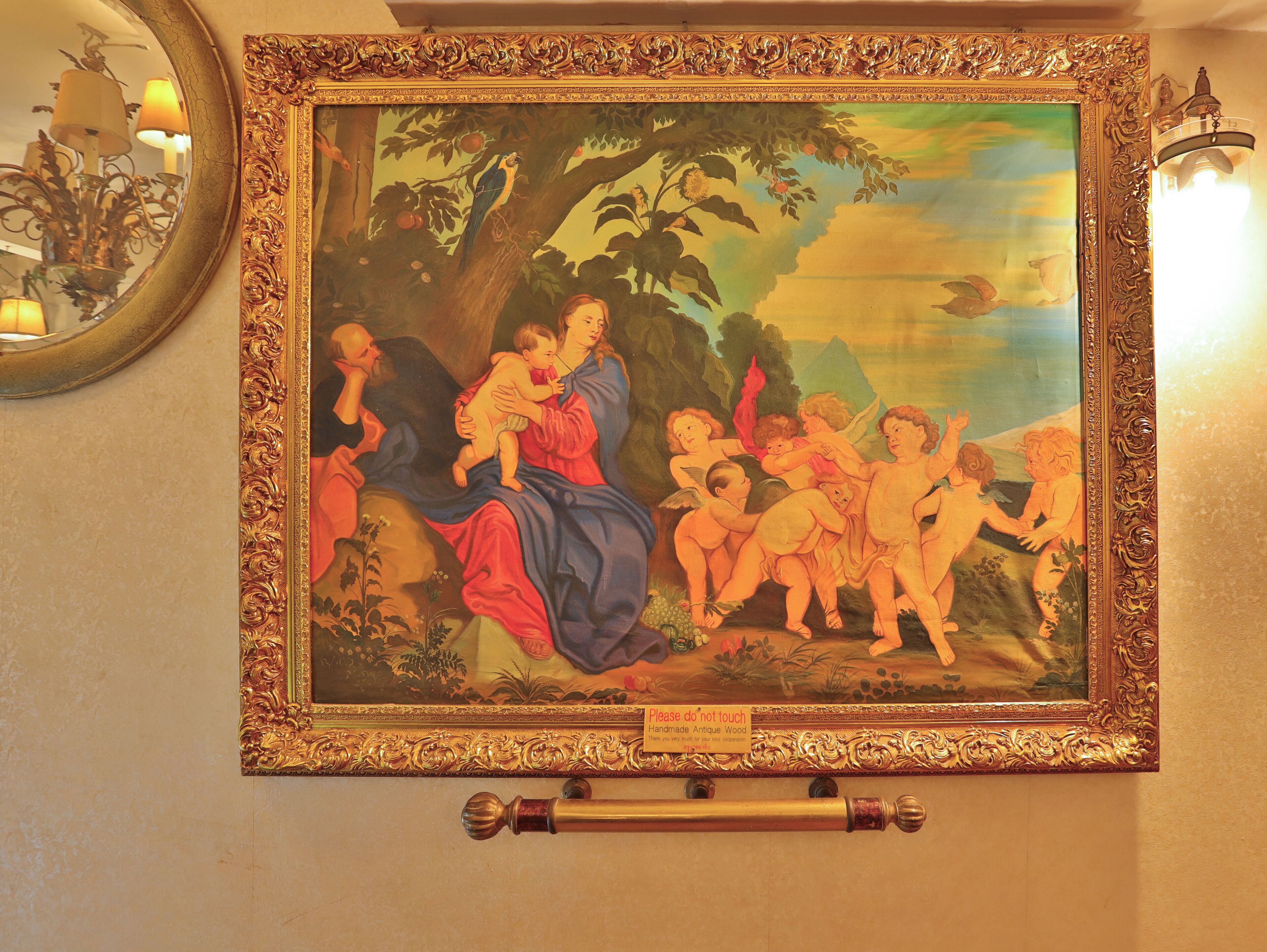 A framed painting with a 'Please do not touch' sign, a decorative mirror, and a chandelier.