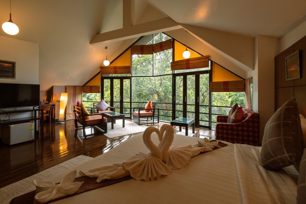 Une chambre d’hôtel avec un grand lit, une télévision, un bureau et un coin salon avec vue sur les arbres.