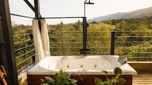 Een bubbelbad op een balkon met uitzicht op groen en heuvels.