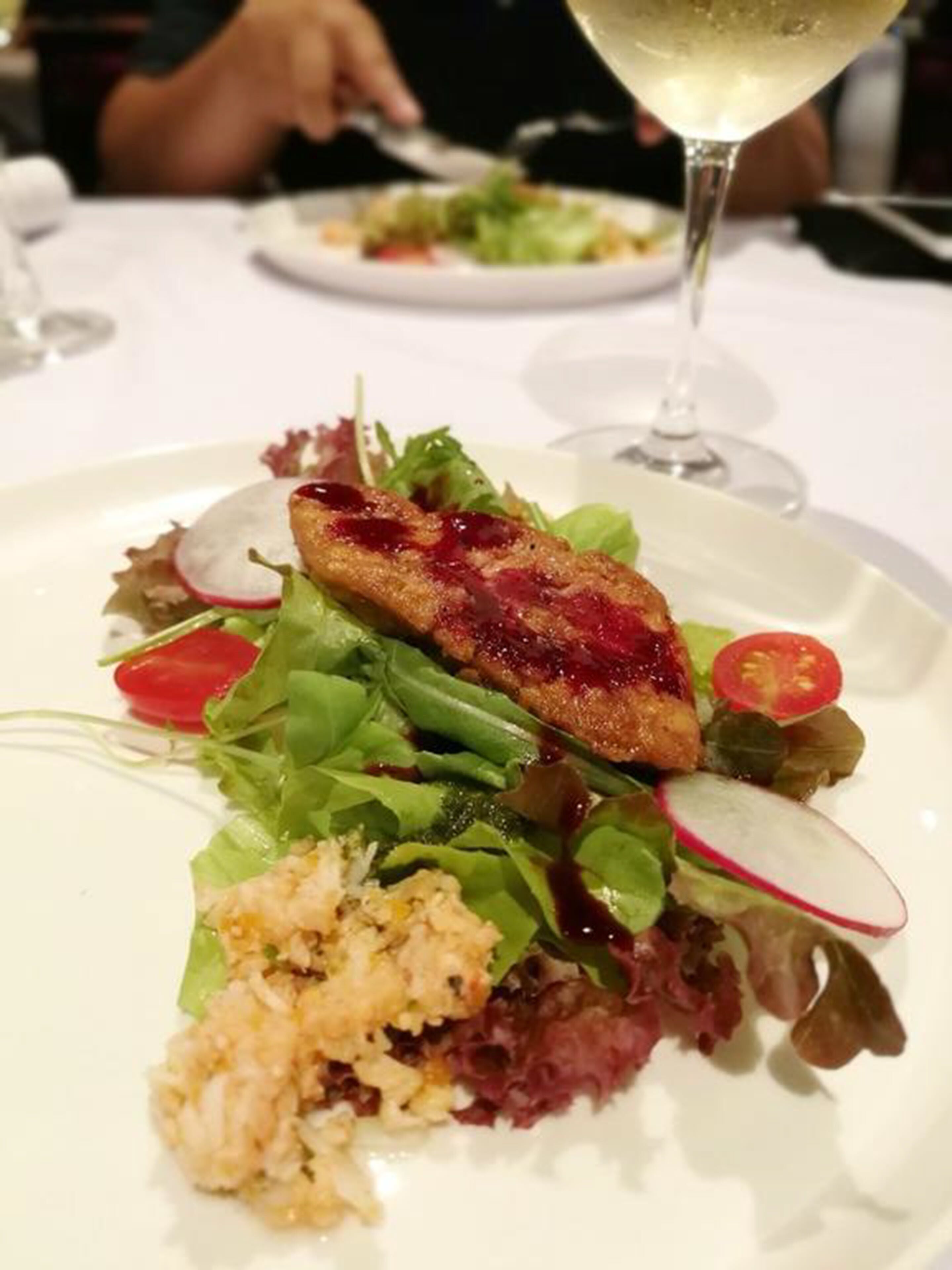 A plate of food with a salad, a slice of meat, and a glass of white wine.
