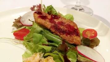 A plate of food with a salad, a slice of meat, and a glass of white wine.