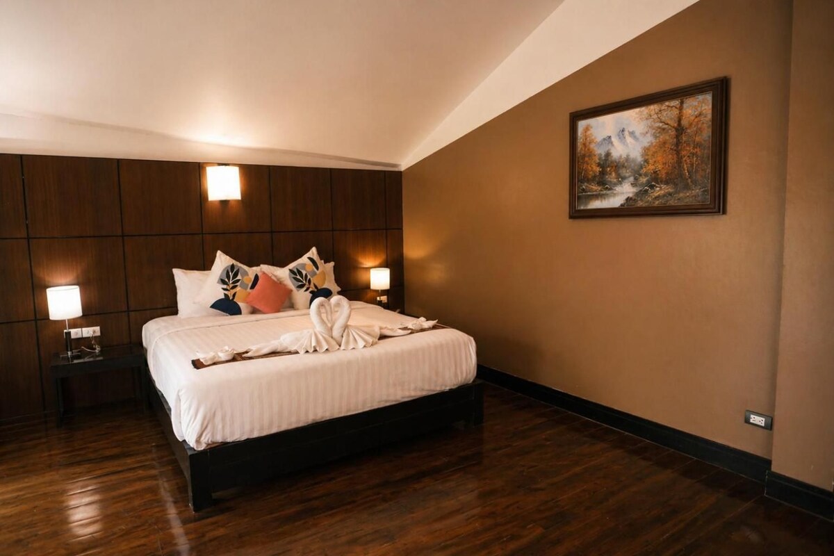 A hotel room with a large bed, wooden headboard, two bedside lamps, and a painting on the wall.