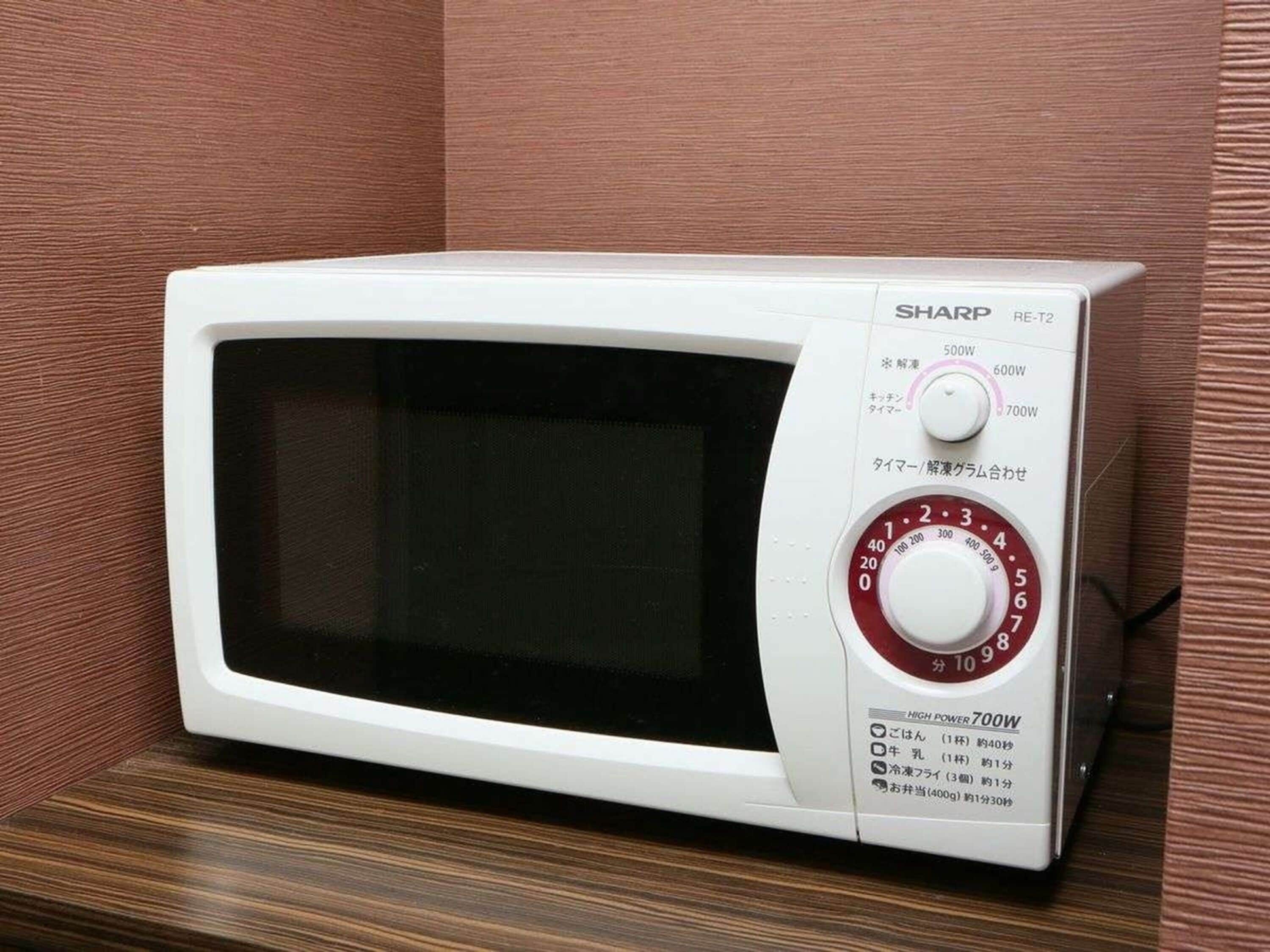 A white Sharp microwave oven with a digital display and a red power dial, placed on a wooden surface.