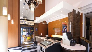 A hotel reception area with a check-in counter, a digital kiosk, and a seating area with a checkered floor. - APA Hotel Chiba Yachiyo Midorigaoka (Yachiyo)