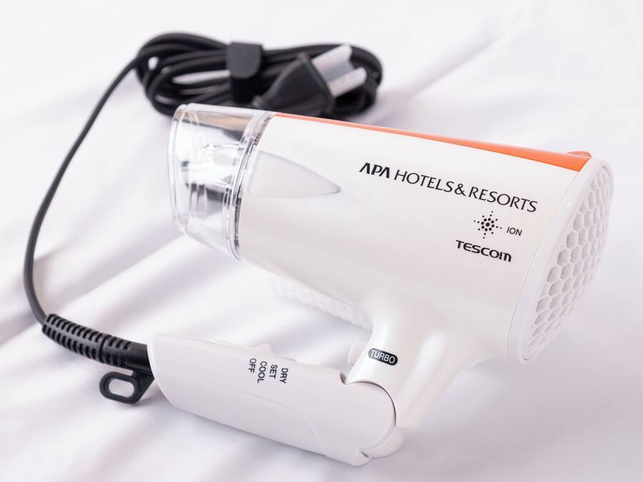 A white hair dryer with a black cord and a clear protective cover.