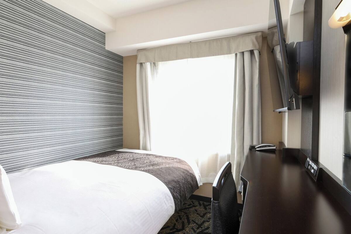 A hotel room with a bed, a desk, a television, and a window with curtains.