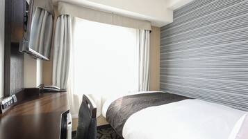 Quarto de hotel com escrivaninha, cadeira, cama e uma janela grande com cortinas.