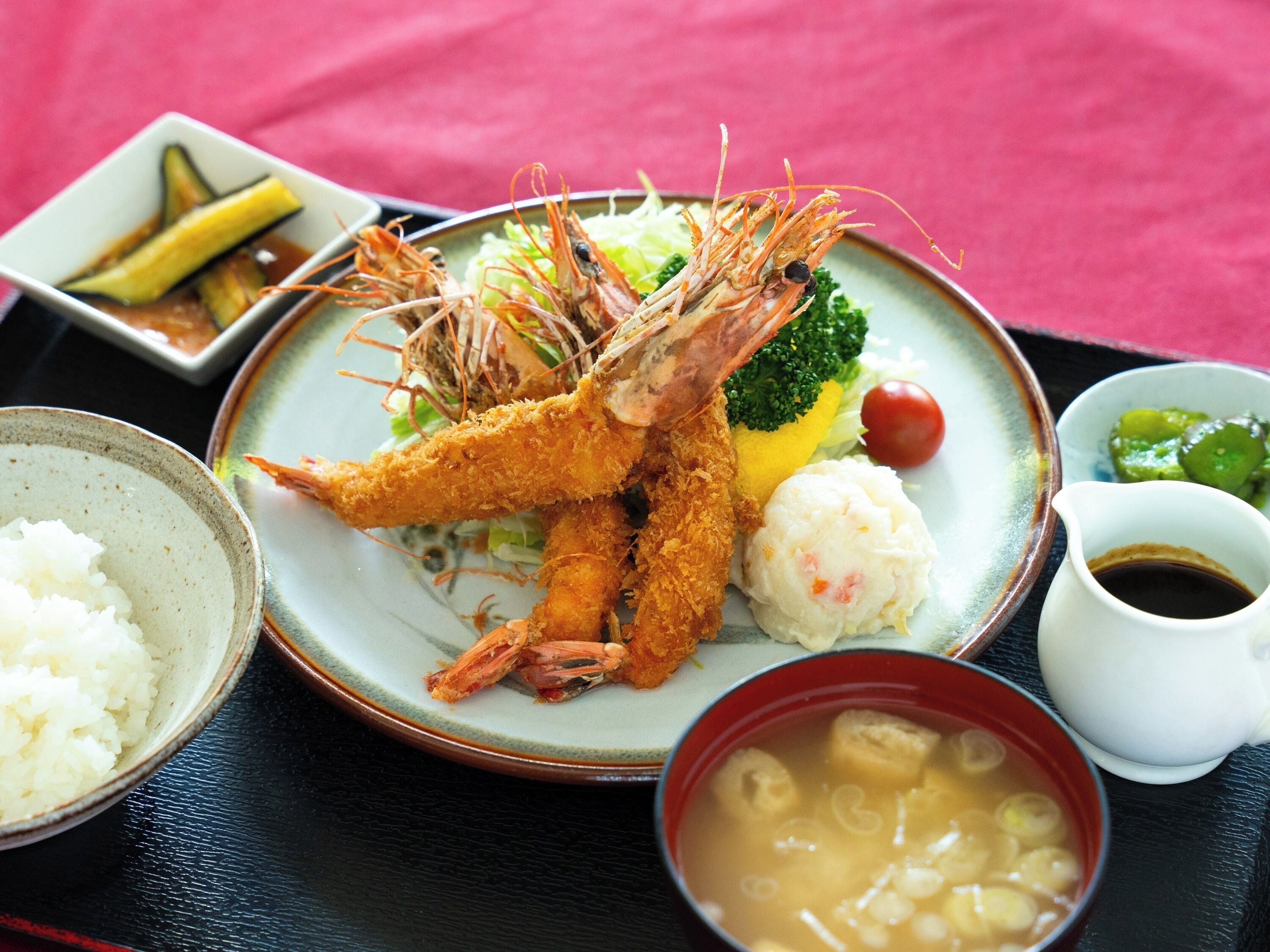 A plate of fried shrimp with vegetables and rice, accompanied by a small bowl of soup and a cup of soy sauce.