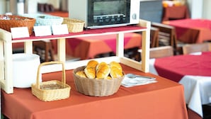 Een ontbijt opstelling met een broodrooster, broden in manden en een mand met sinaasappels op een tafel.