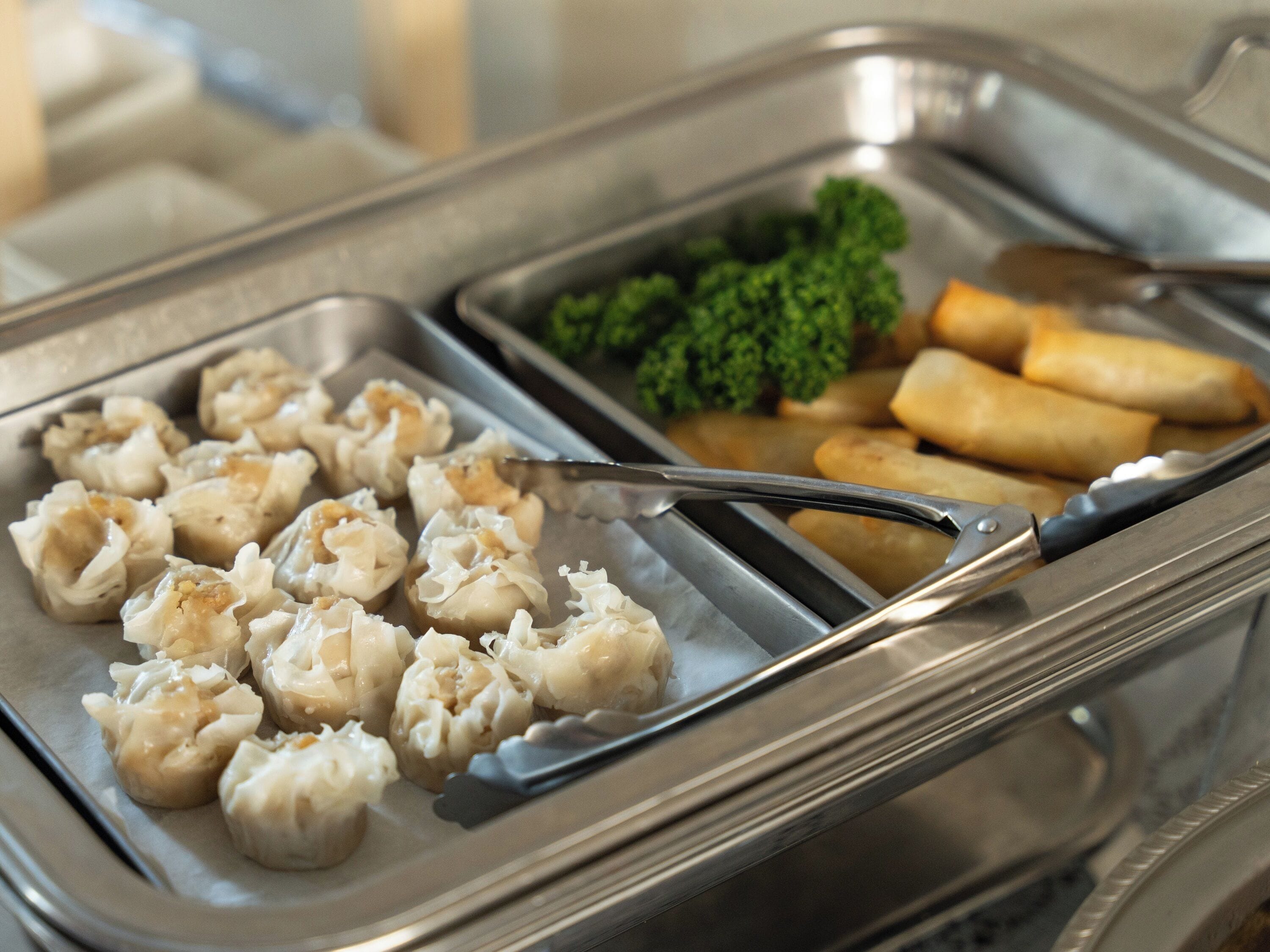 A buffet with dumplings, broccoli, and spring rolls.