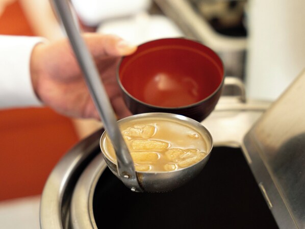 A person holding a ladle over a pot, with a red bowl in the background.