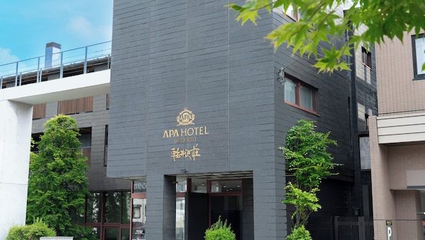Een modern gebouw met een donkere gevel en een bord waarop 'APA HOTEL' staat.