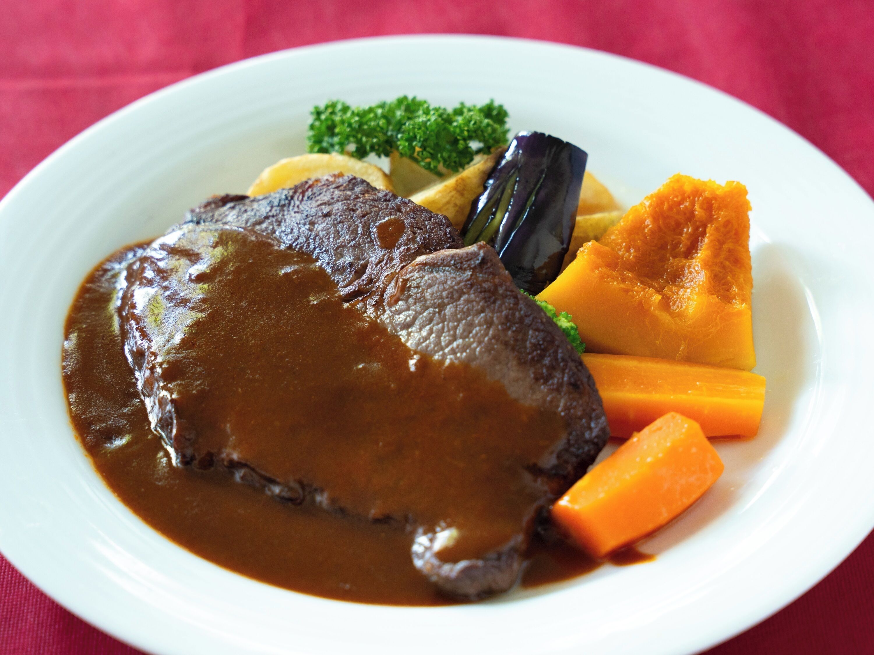 A plate with a beef steak, gravy, carrots, and a piece of eggplant.