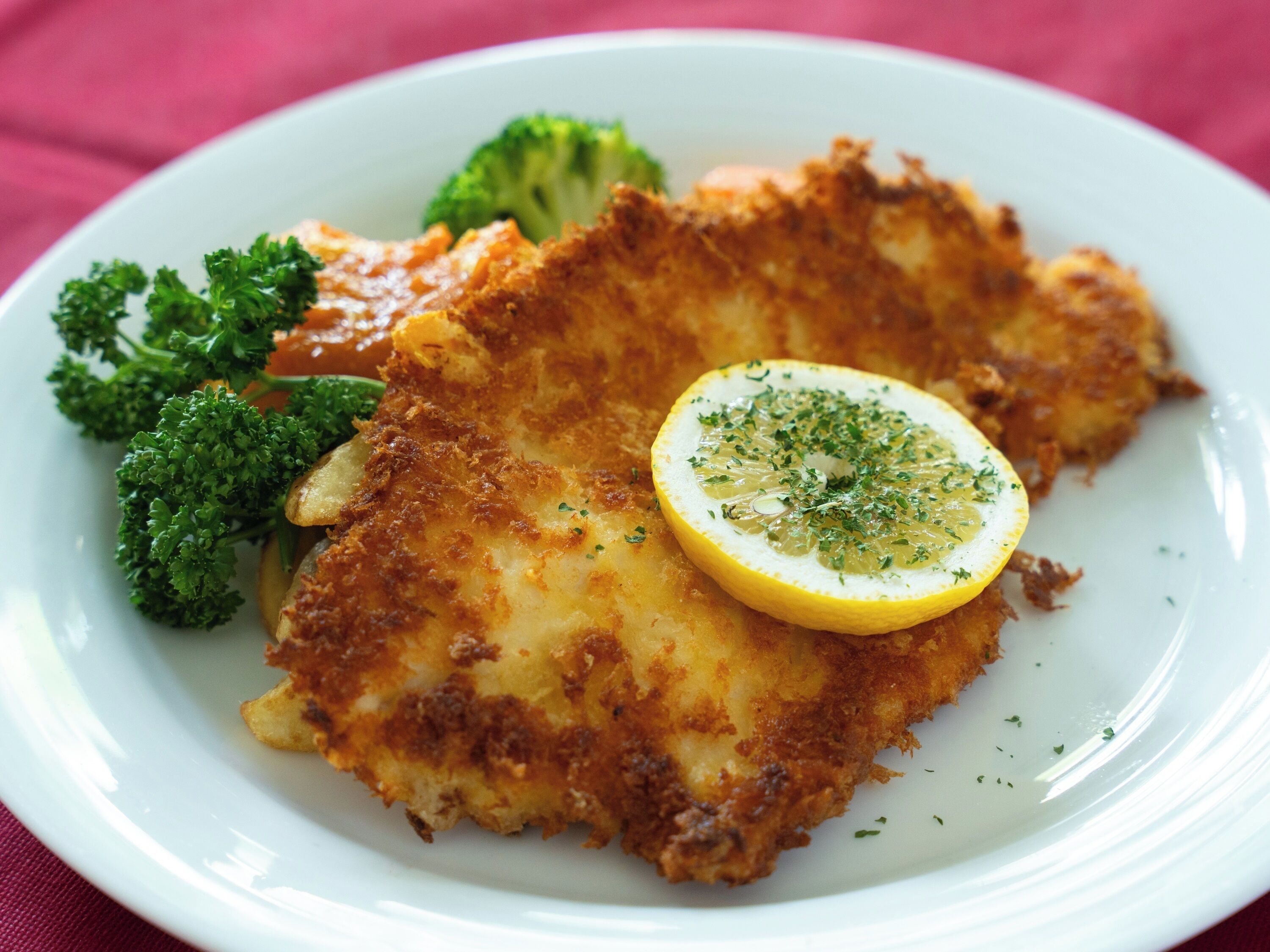 Un plato con una milanesa, una rodaja de limón y brócoli.