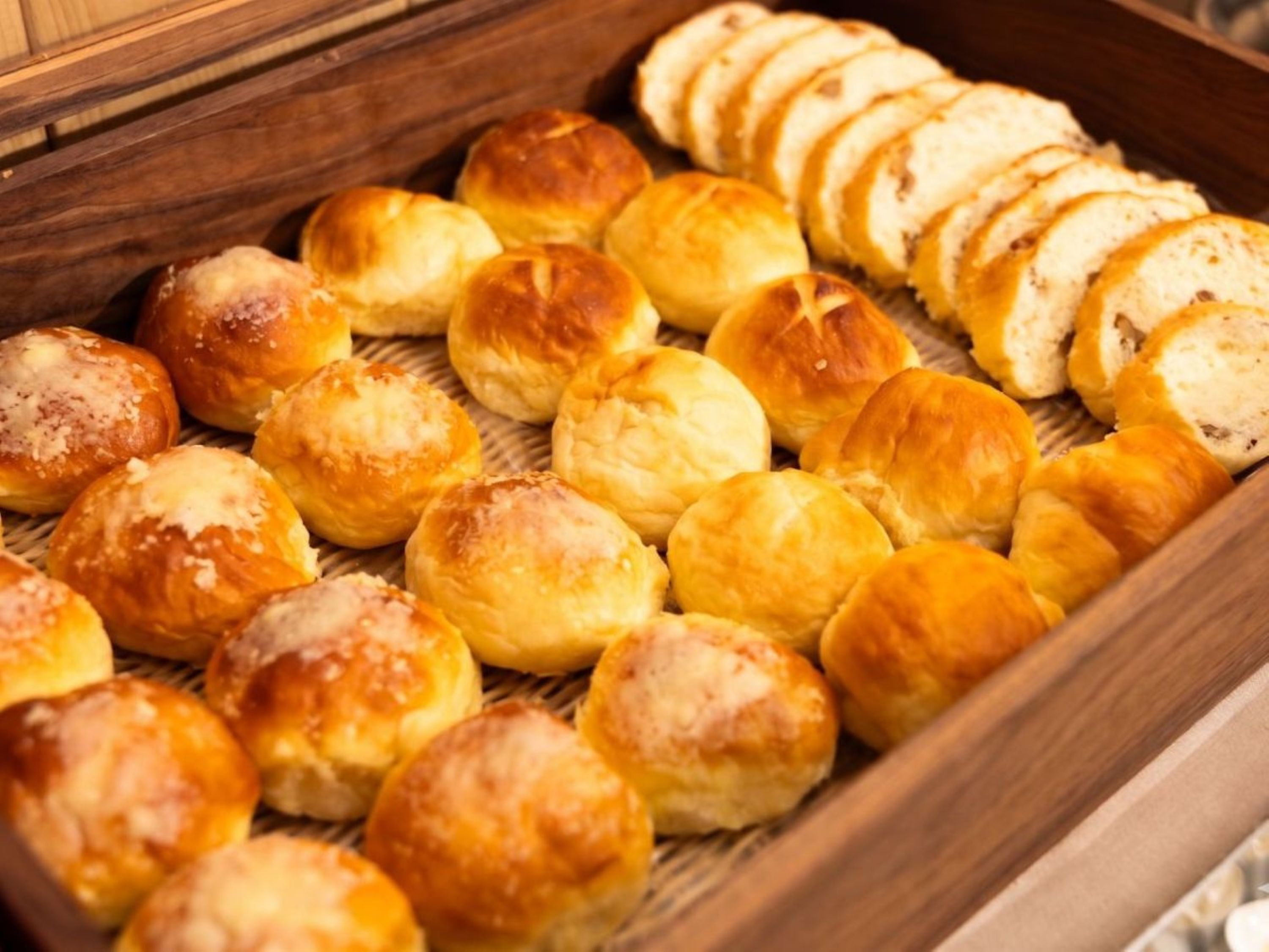 A wooden tray filled with various baked goods, including rolls and sliced bread.
