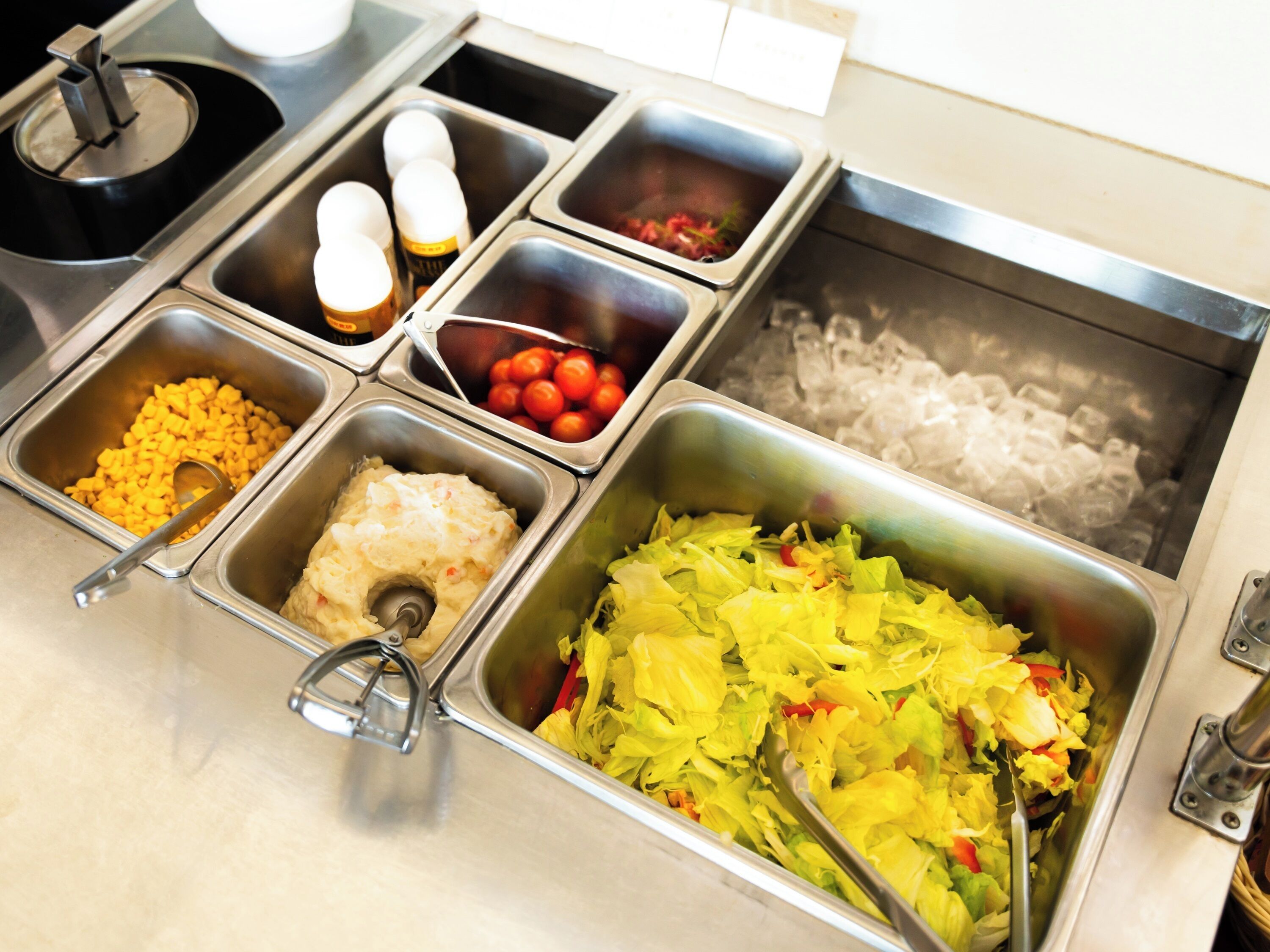Un buffet con diverse opzioni alimentari tra cui pasta, insalata e un contenitore di ghiaccio.