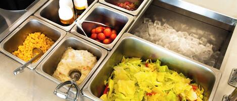 A buffet with various food options including pasta, salad, and a container of ice.