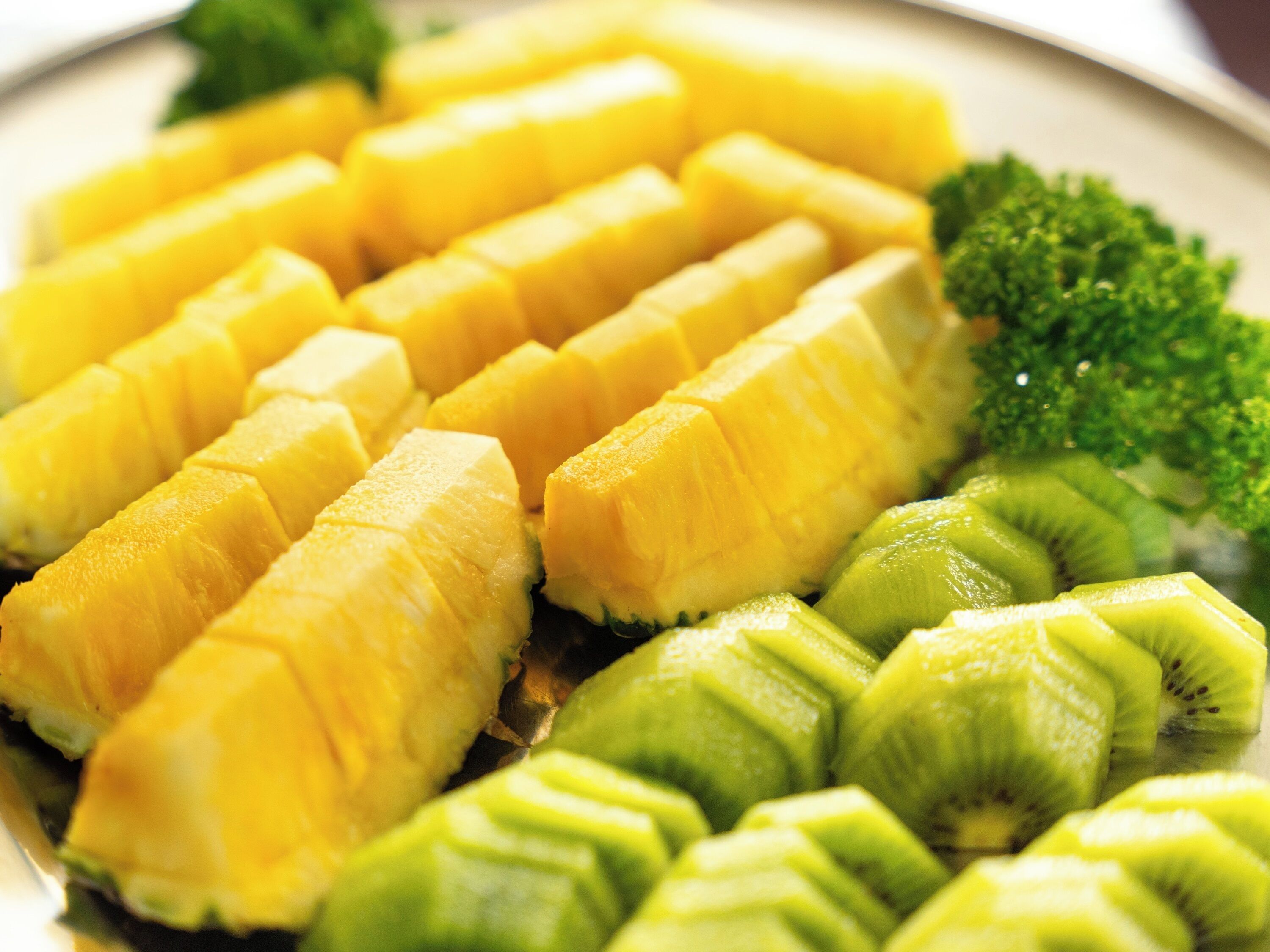 A plate with neatly arranged pineapple chunks and kiwi slices, garnished with a sprig of broccoli.