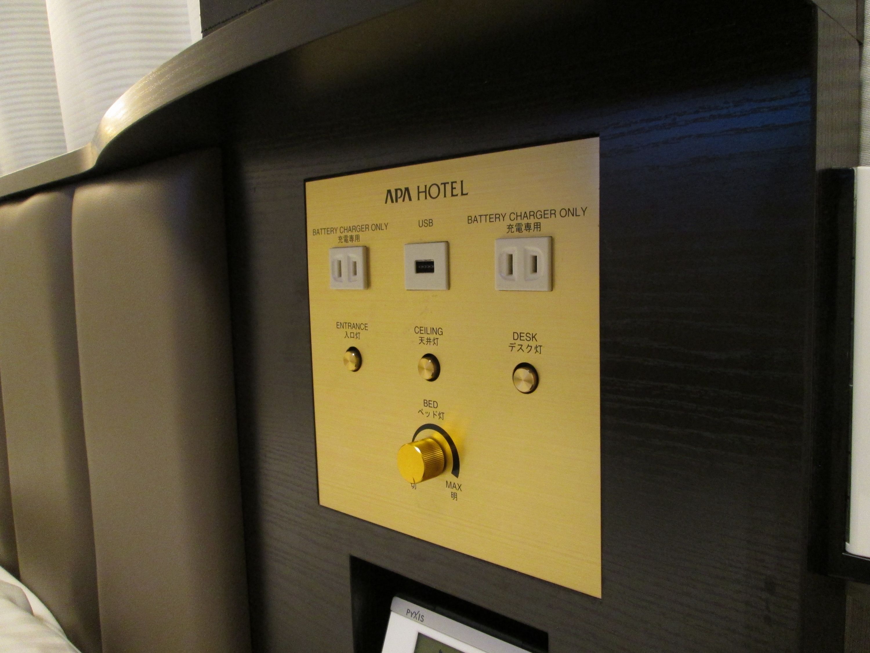 A control panel with battery charger, USB port, and switches for entrance, ceiling, desk, and bed lighting at APA Hotel.