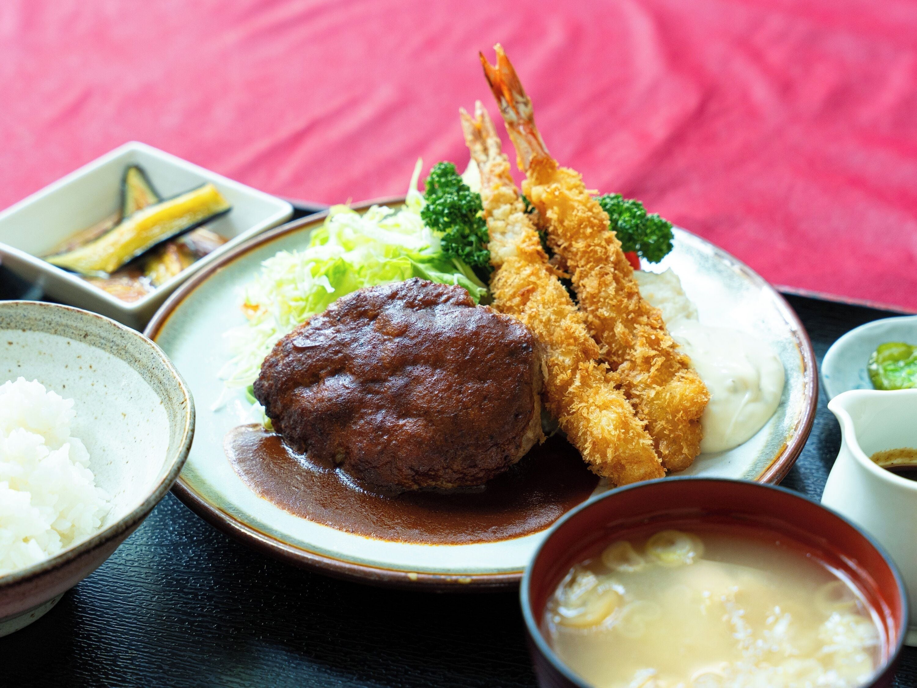 A plate of food including tempura shrimp, a meatball, and vegetables.