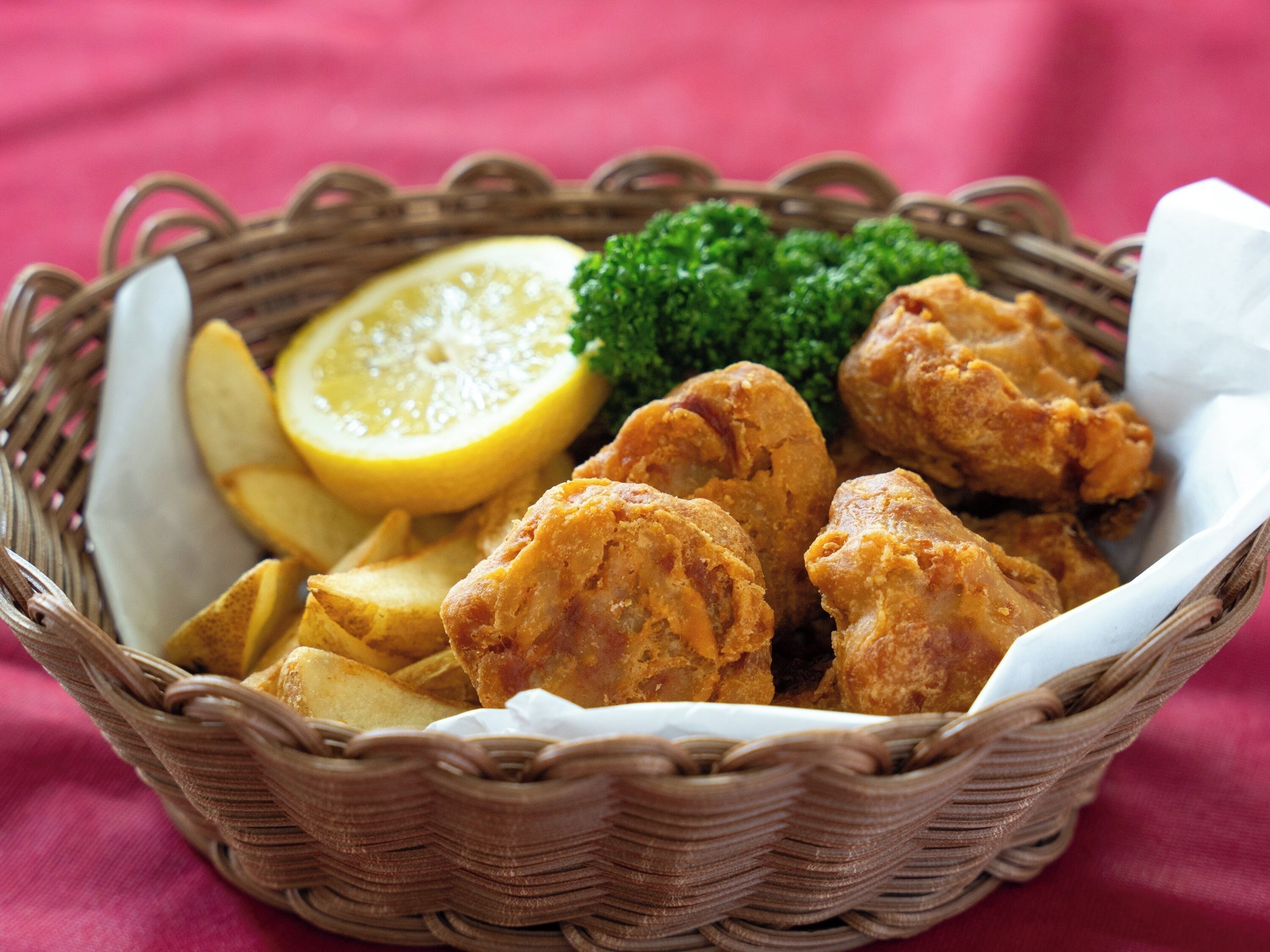A basket containing fried chicken, lemon slices, and potatoes.