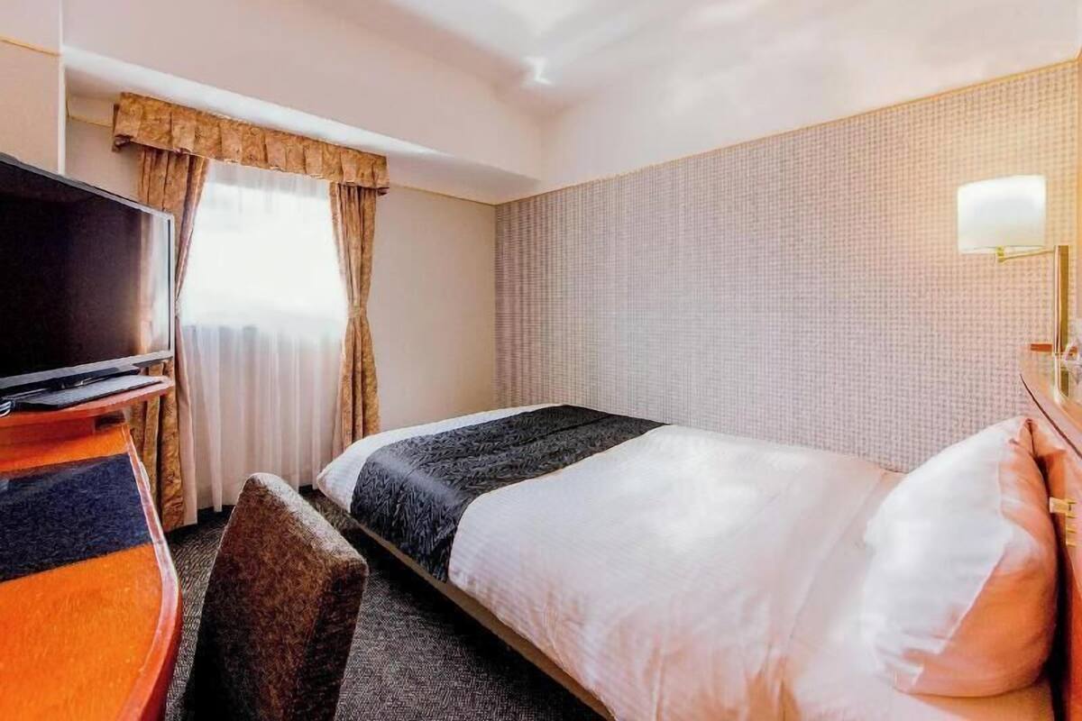 Habitació d'hotel amb un llit, una televisió, un escriptori i una làmpada.