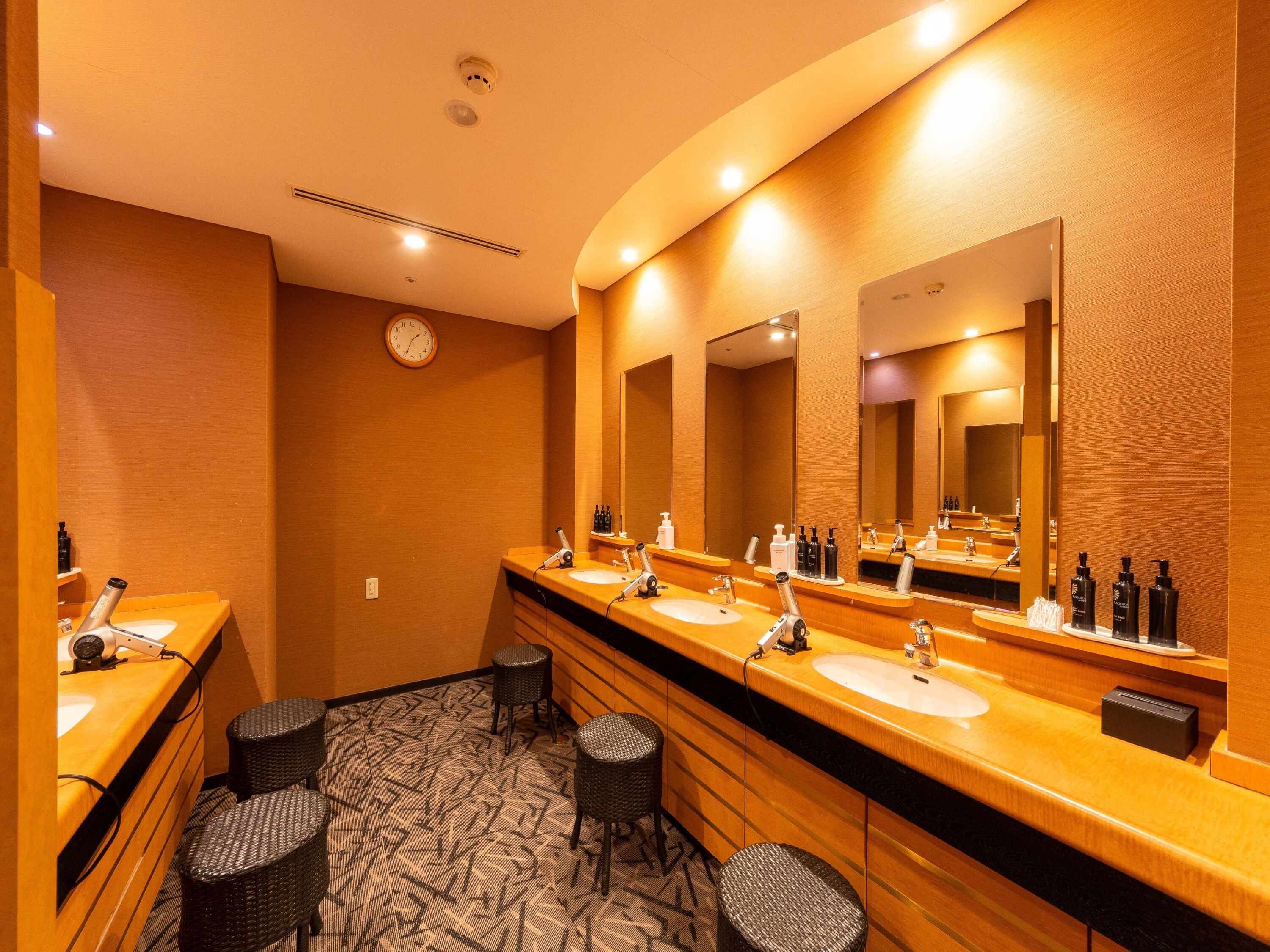 Une salle de bain d’hôtel avec deux lavabos, un grand miroir et une horloge au mur.
