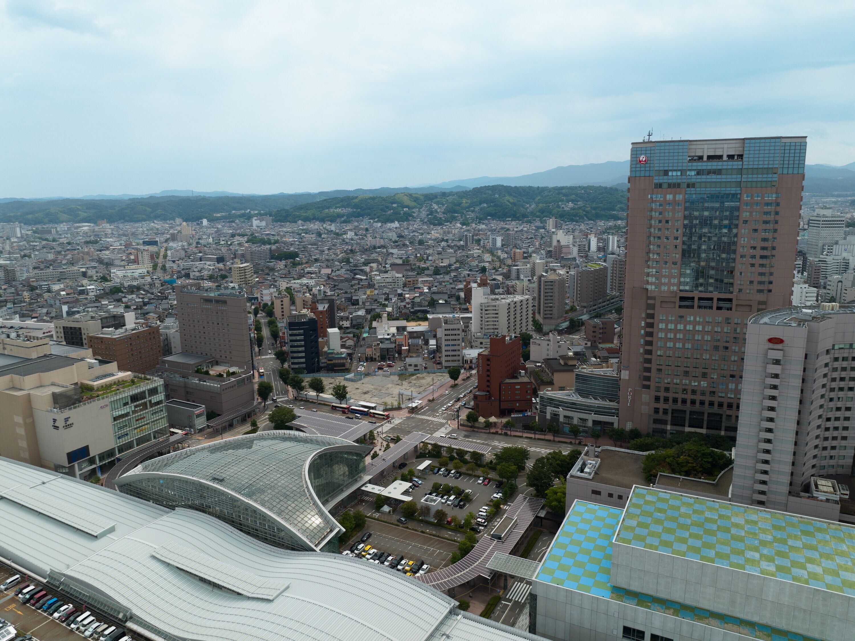 A cityscape with a mix of modern and traditional buildings, a prominent curved glass structure, and a large building with a checkered roof.