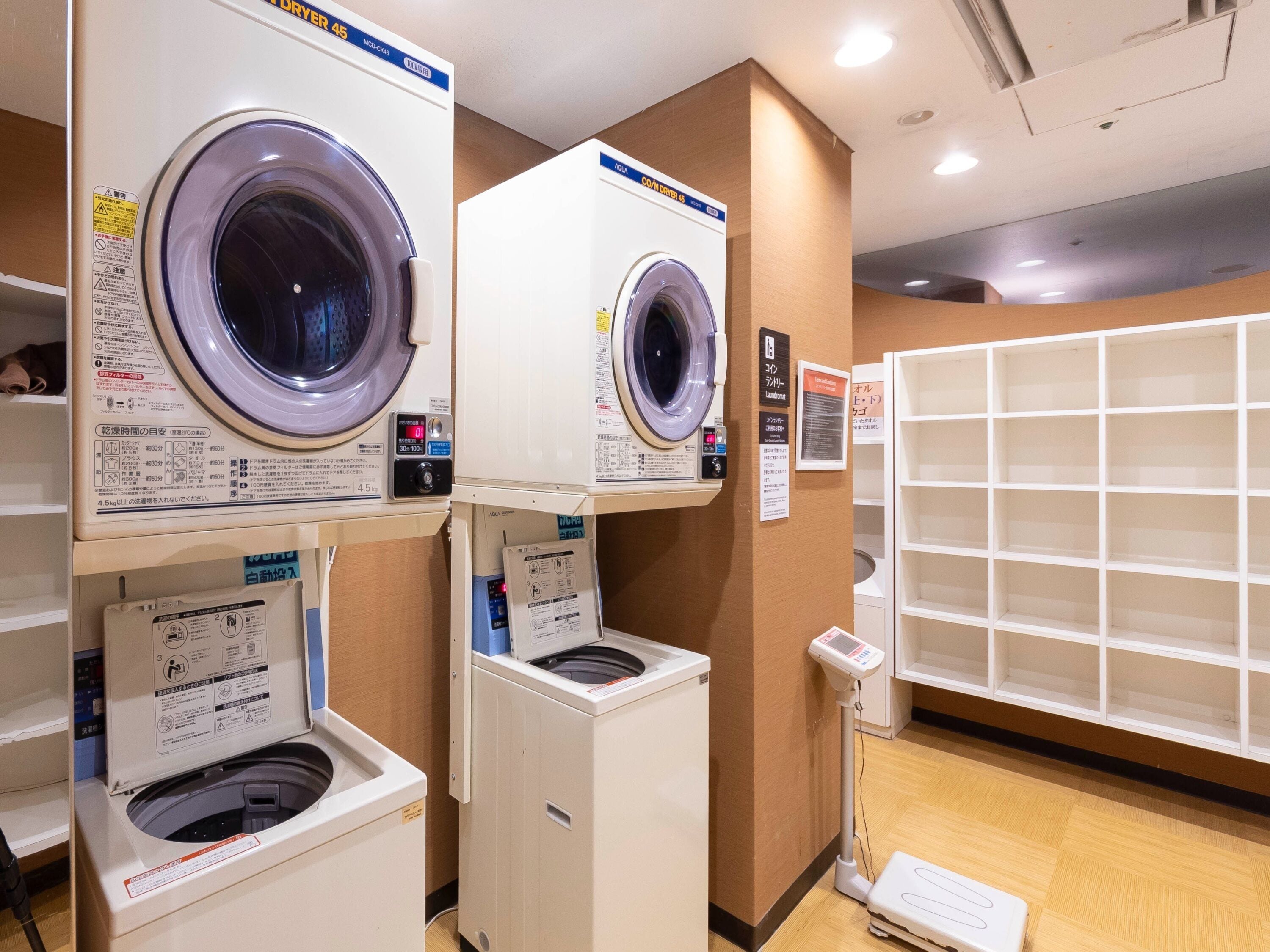 Une laverie équipée de plusieurs machines à laver et de plusieurs séchoirs, d’une balance pour peser le linge et de panneaux d’information.