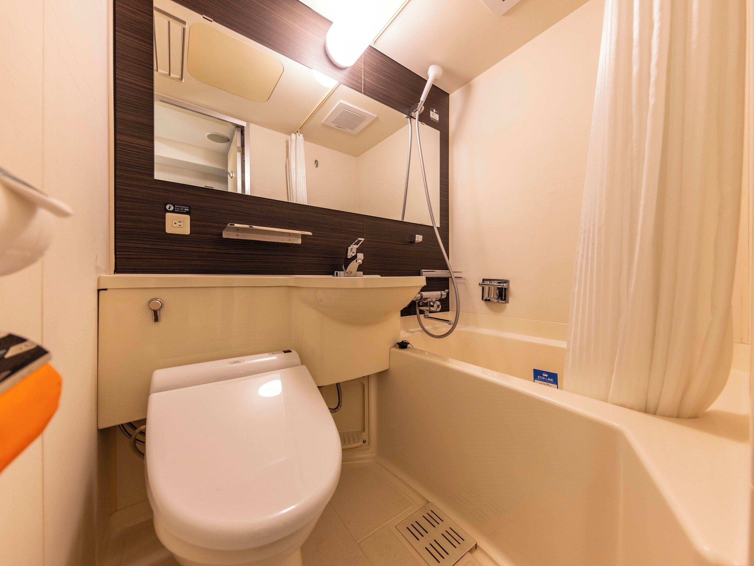 Une petite salle de bain avec des toilettes blanches, un lavabo, un miroir et une douche.