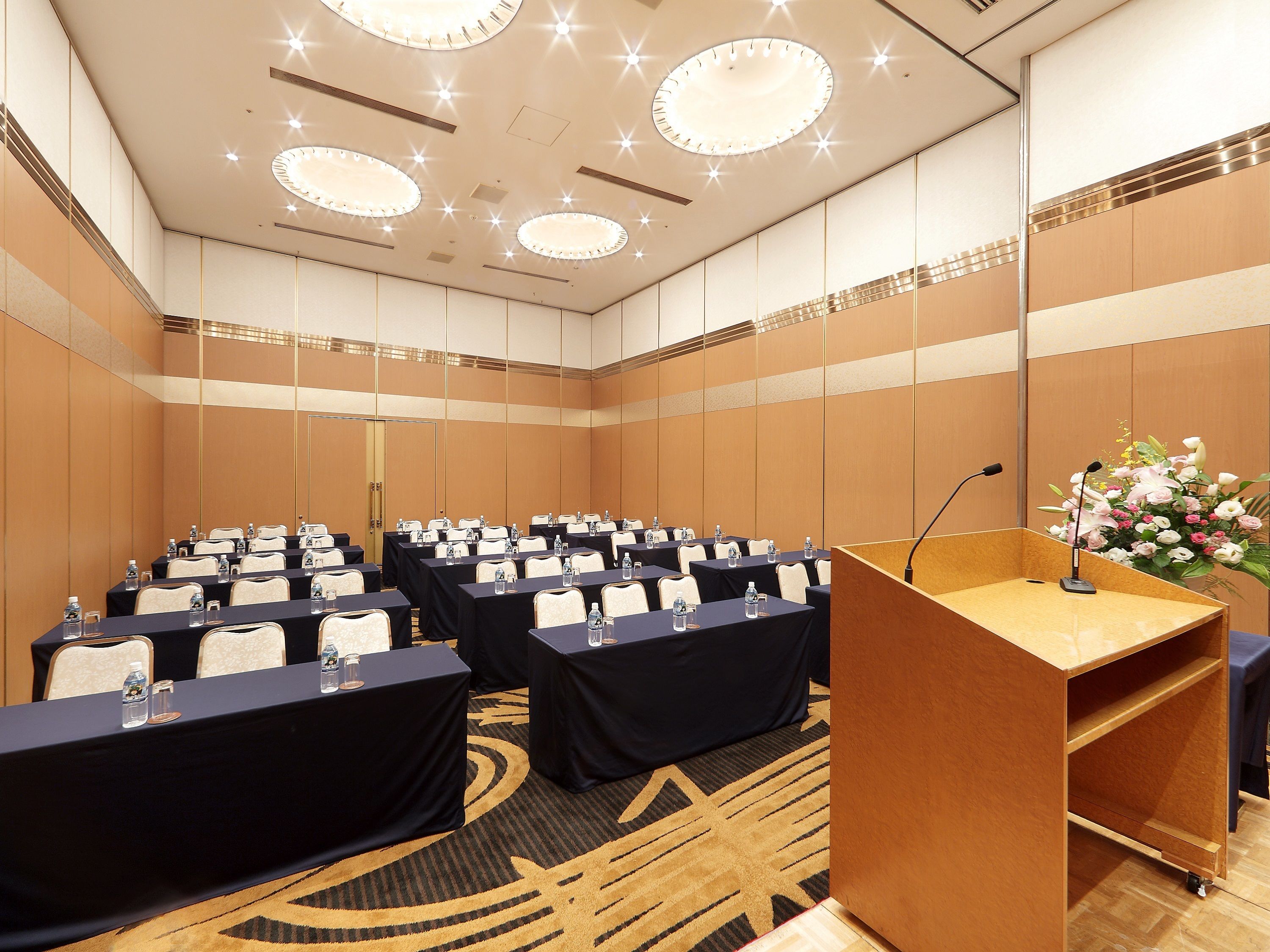 Una sala conferenze con file di tavoli, sedie e un podio con un microfono.